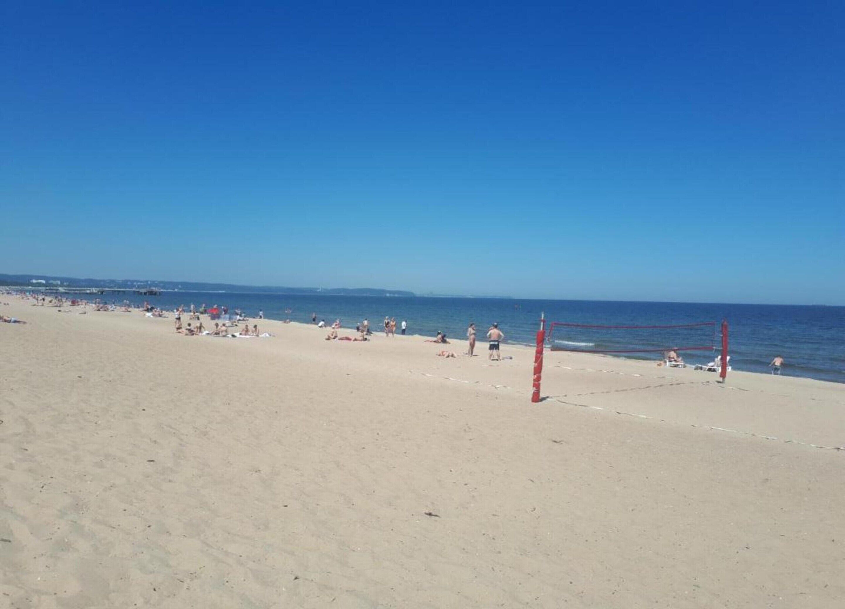 Une plage avec un filet de volley-ball et des gens qui prennent un bain de soleil.