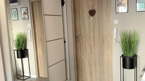 A hallway with a wooden door, two potted plants, and a mirrored closet. - Apartment in Gdynia Near Baltic Beach (Gdańsk)