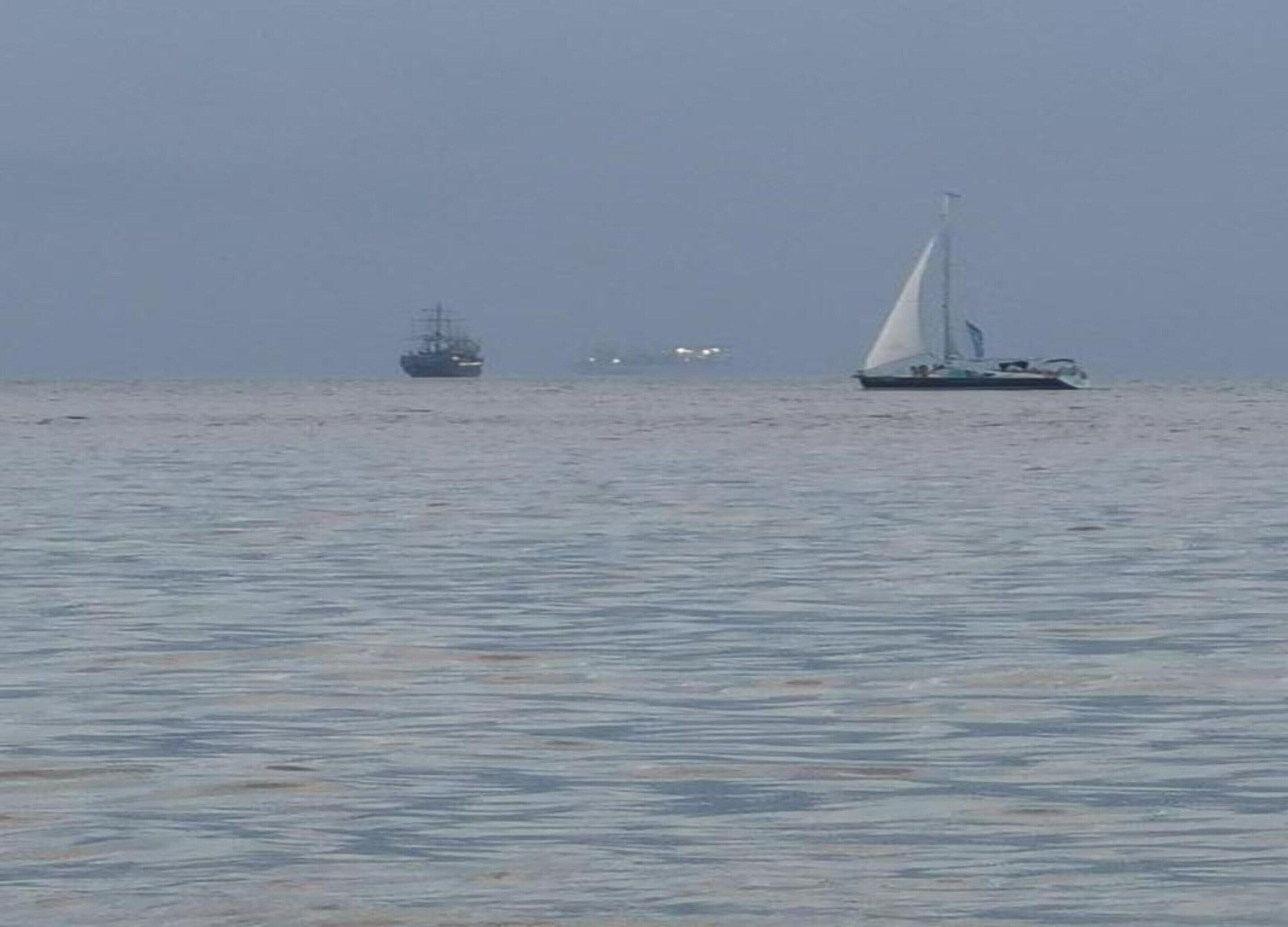 Ett lugnt hav med en segelbåt och ett fartyg i fjärran.