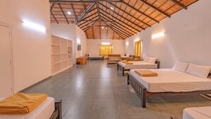 Una habitación amplia con varias camas dispuestas en fila, techo alto con estructura de vigas de madera y un interior luminoso y bien iluminado.