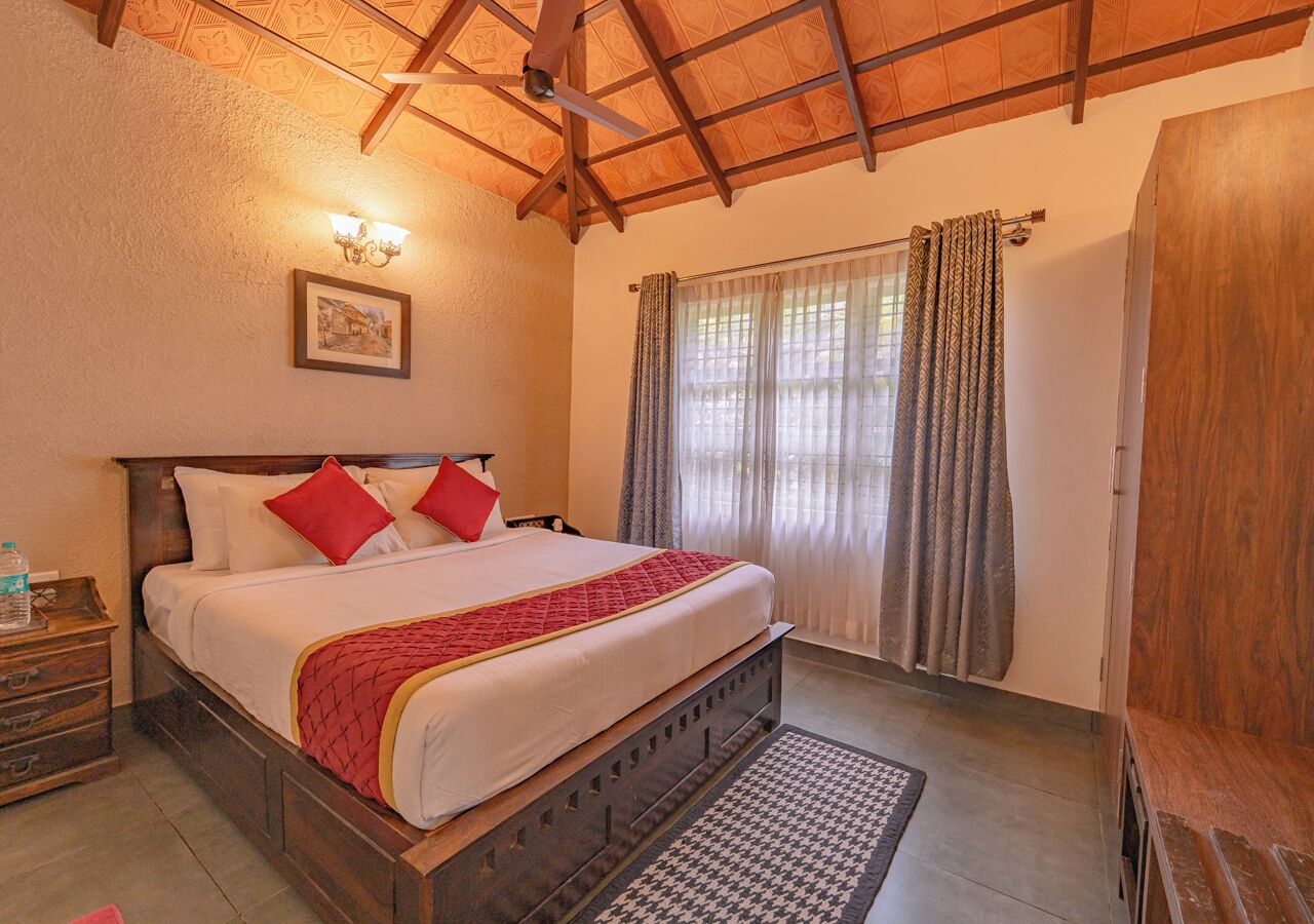 A bedroom with a wooden bed, a nightstand, a wall-mounted light, and a window with curtains.