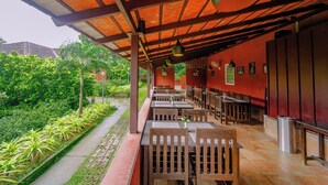 Un restaurante al aire libre con mesas y sillas de madera, un área de estar cubierta y vistas a la vegetación.