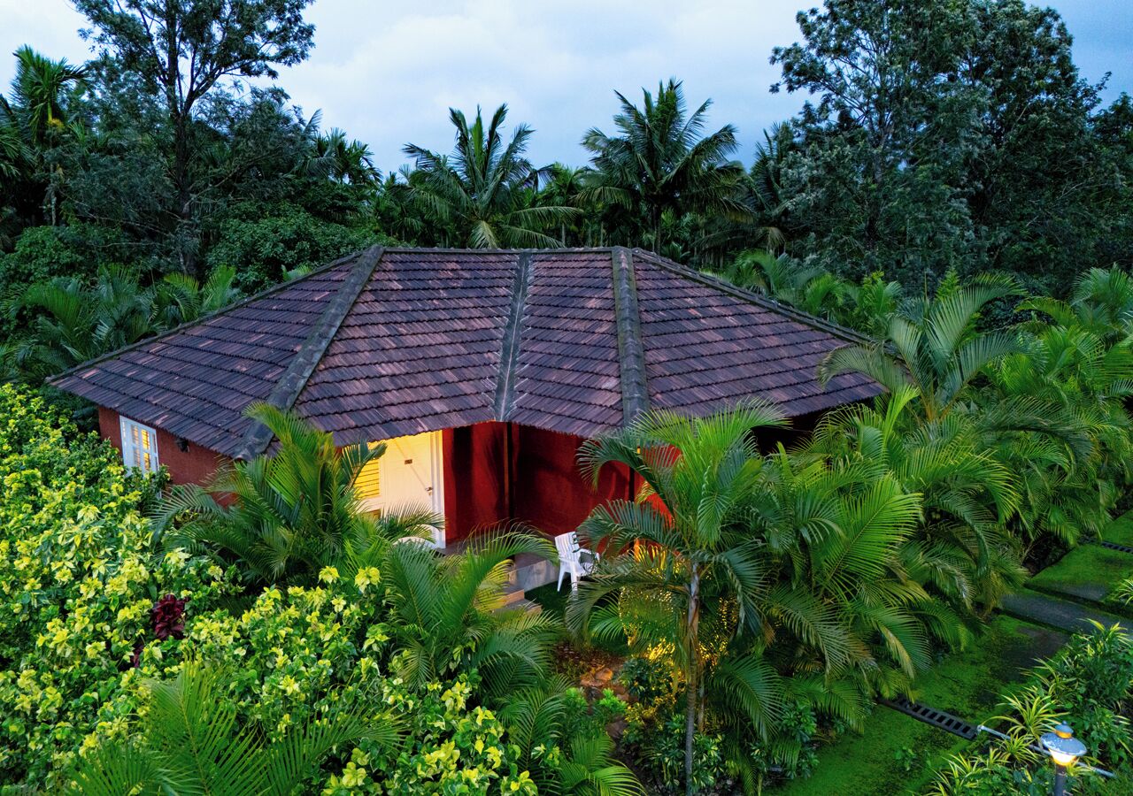 A small, single-story building with a tiled roof surrounded by lush greenery and palm trees.
