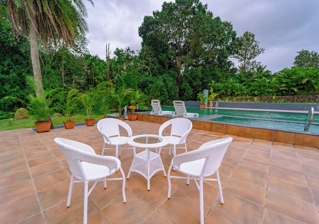 Un patio con mobiliario de mimbre blanco y una piscina.