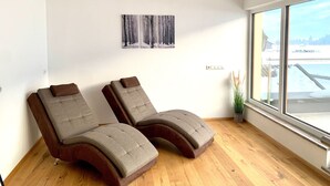 A room with two reclining chairs, a painting of a forest, a window with a view of a bridge, and a ceiling light. - Chalet in Stuhlfelden Near Ski Slopes (Mittersill)