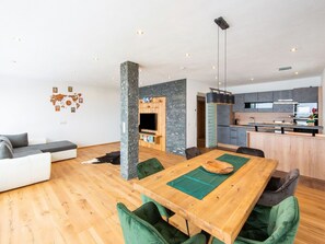 Un espacio habitable moderno con una mesa de comedor de madera, sillas tapizadas en verde, un sofá gris y una zona de cocina con armarios grises y una encimera negra.