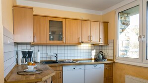 A compact kitchen with wooden cabinets, a dishwasher, and a window with a stone wall view.