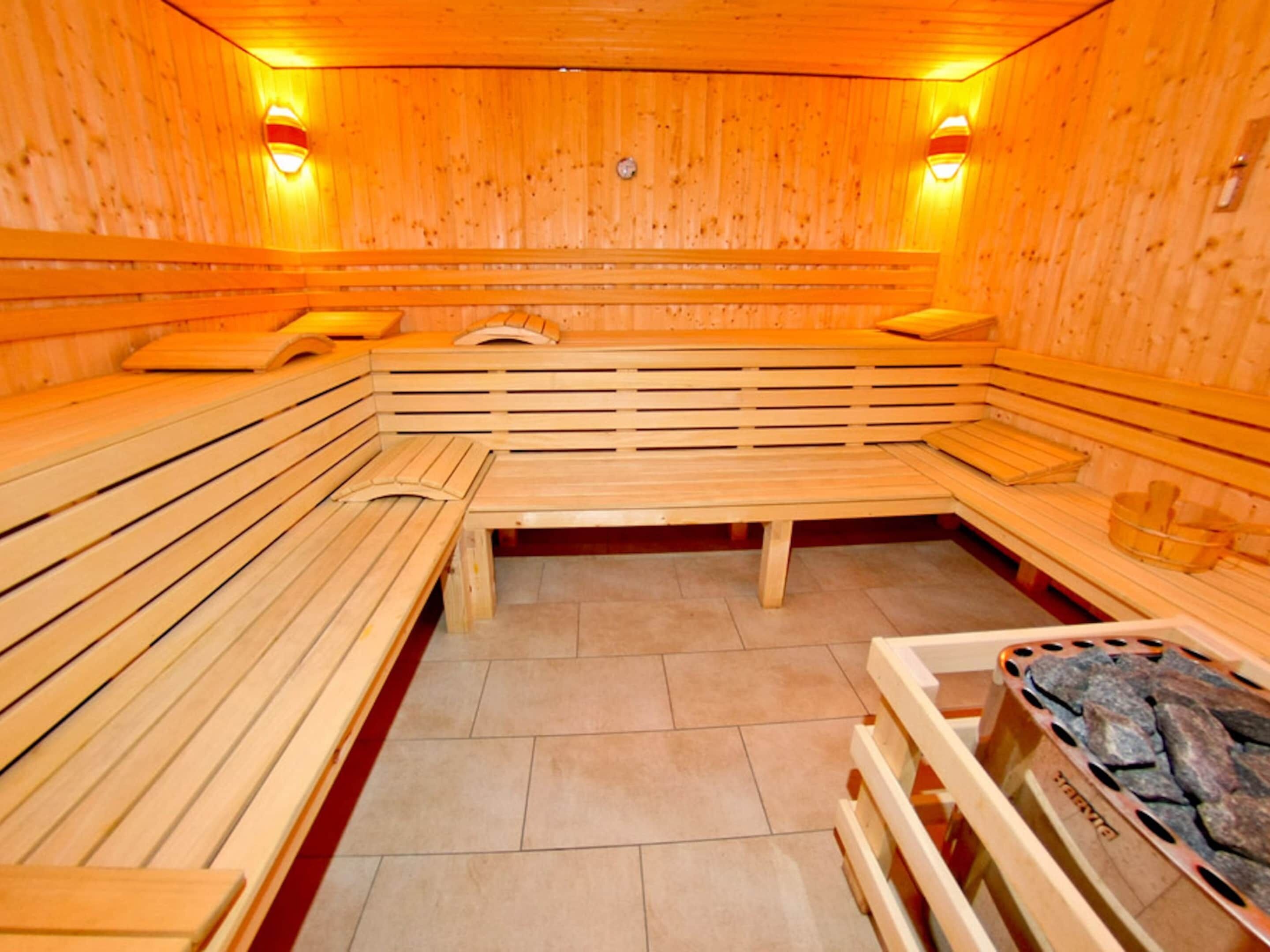 A sauna with wooden benches and benches, tiled floor, and wall-mounted lights.
