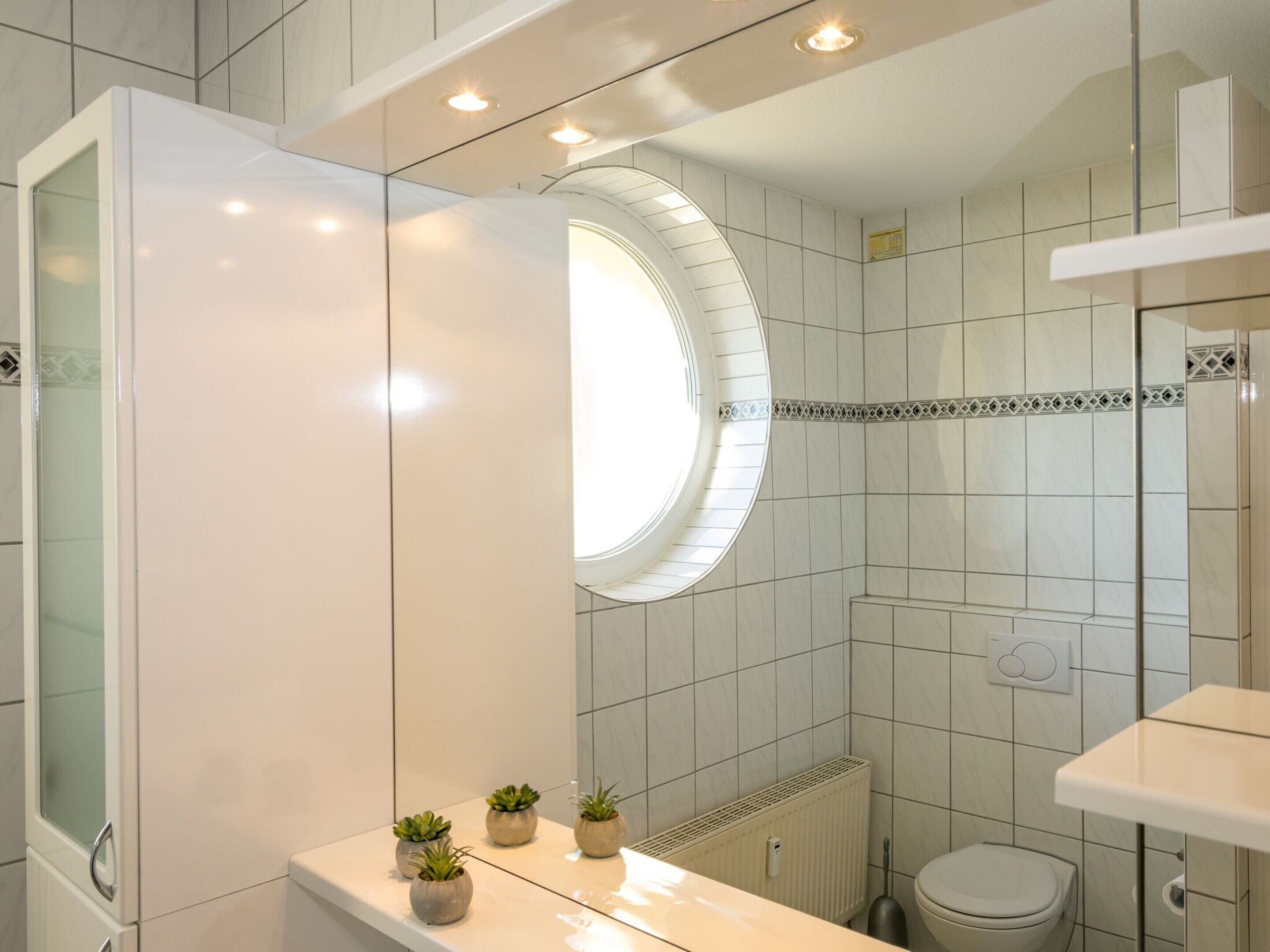 Een moderne badkamer met een glazen douchecabine, een rond dakraam en een witte wastafel met potplanten.