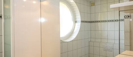 Een moderne badkamer met een glazen douchecabine, een rond dakraam en een witte wastafel met potplanten.