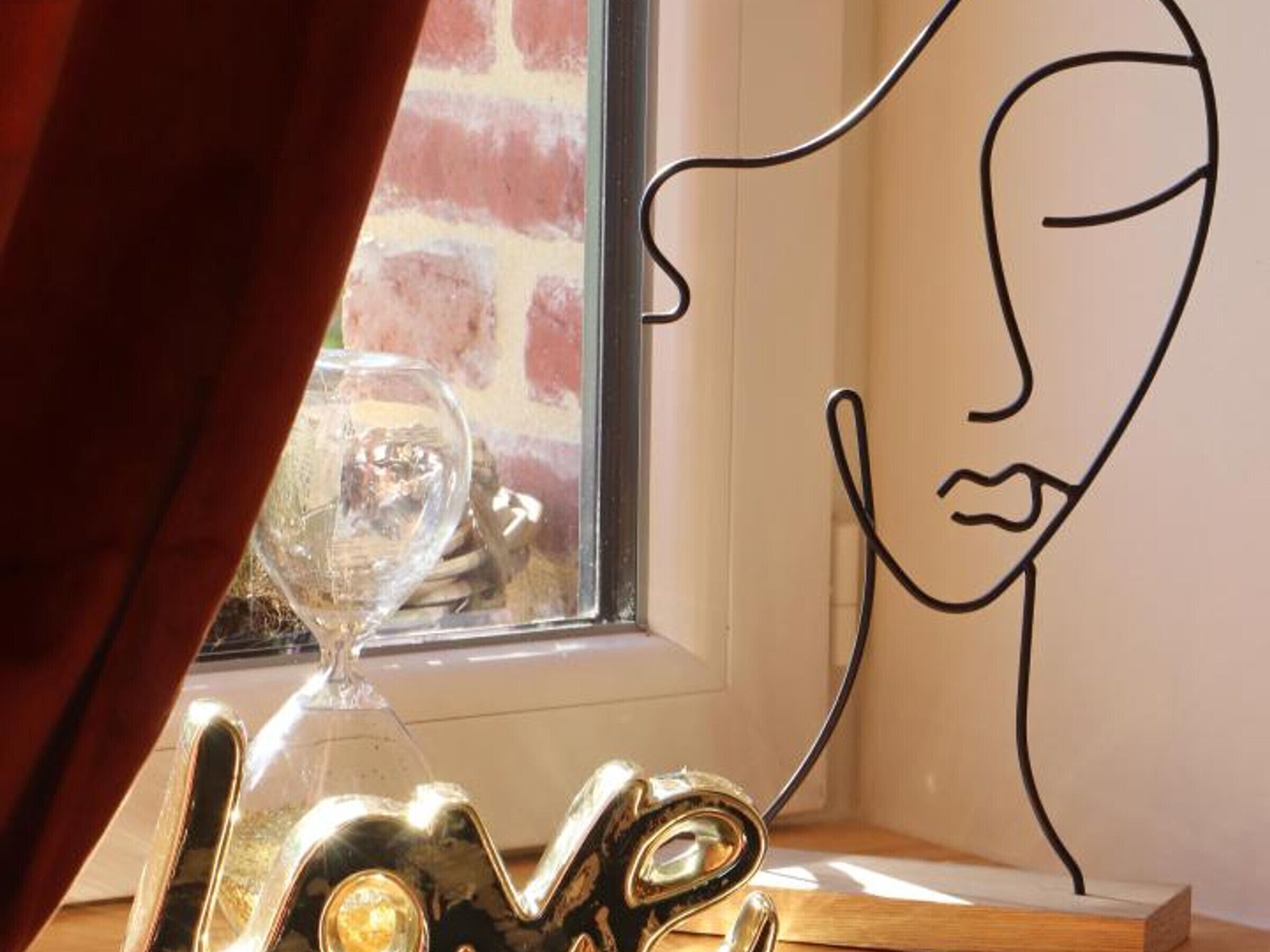Una habitación con ventanal, una escultura de vidrio y un dibujo lineal de un rostro en la pared.