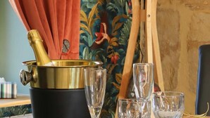 Une table sur laquelle se trouve une bouteille de champagne dans un seau doré, entourée de verres vides, le tout sur fond d’un tableau coloré et d’un chevalet en bois.