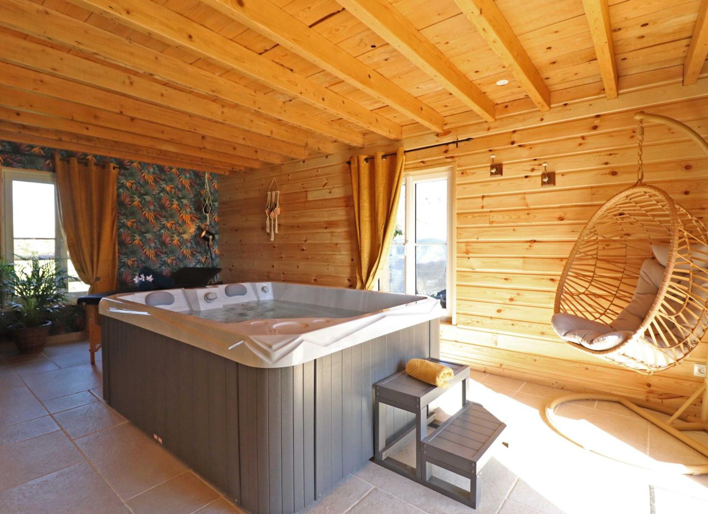 Een houten chalet met een jacuzzi, een hangstoel en een klein tafeltje met een handdoek.