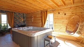 Een houten chalet met een jacuzzi, een hangstoel en een klein tafeltje met een handdoek.