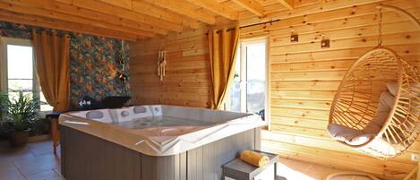 A wooden cabin with a hot tub, a hanging chair, and a small table with a towel.