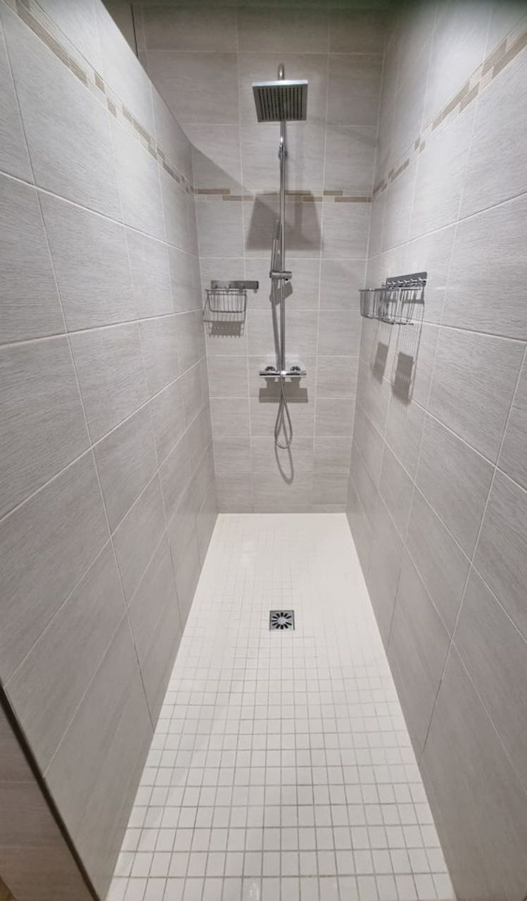 A shower with a handheld showerhead and a fixed showerhead mounted on the wall.
