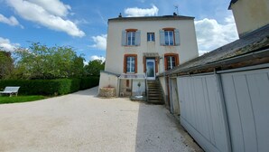 A two-story building with a gravel driveway, a small garden area, and a bench.