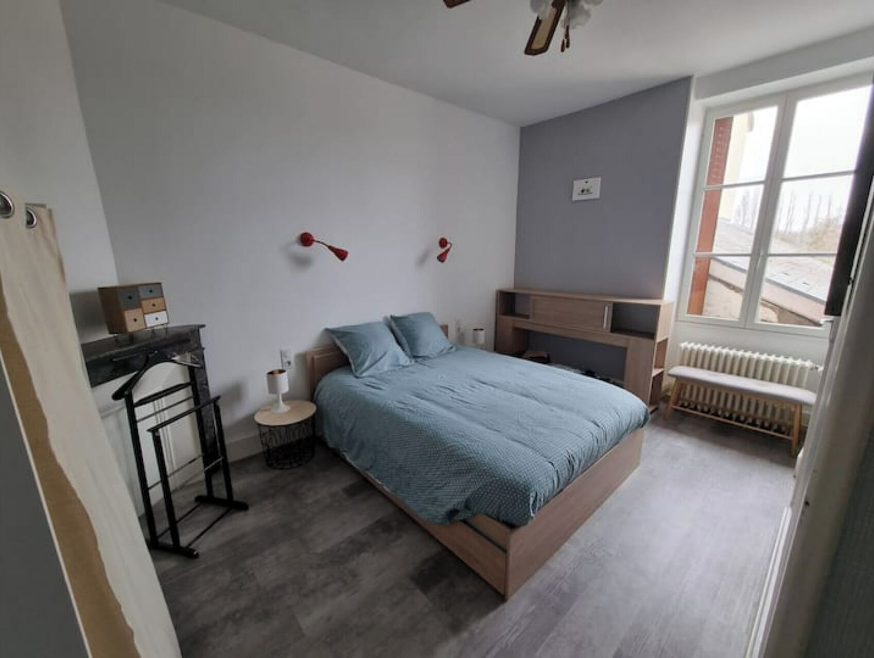 A bedroom with a bed, a desk, a chair, a radiator, and a window.