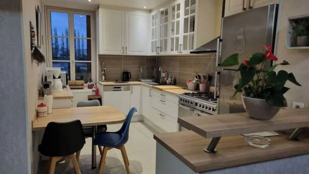A modern kitchen with white cabinets, a stainless steel refrigerator, and a dining area with a table and chairs.
