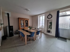 Een eetruimte met een houten tafel en stoelen, een kast met glazen deuren, een klok aan de muur en een raam met uitzicht.
