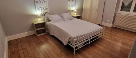 Un dormitorio con cama, suelo de madera, un radiador y una ventana.