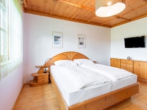 A bedroom with a wooden bed, a nightstand, a TV, and a window with sheer curtains. - Cosy Apartment With Tiled Stove (Radstadt)