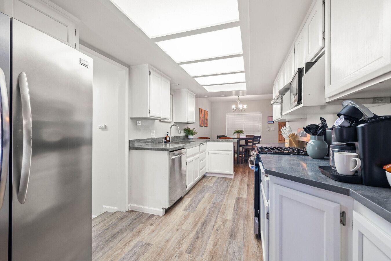 Una cocina moderna con armarios blancos, un refrigerador de acero inoxidable, una isla central con pileta y un comedor con mesa y sillas.