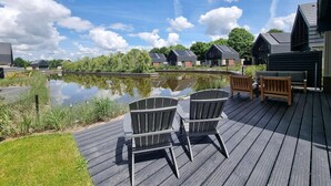 A deck with outdoor seating, a calm water body, and modern buildings in the background. - Waterfront Villa w/ Jetty (Balk)