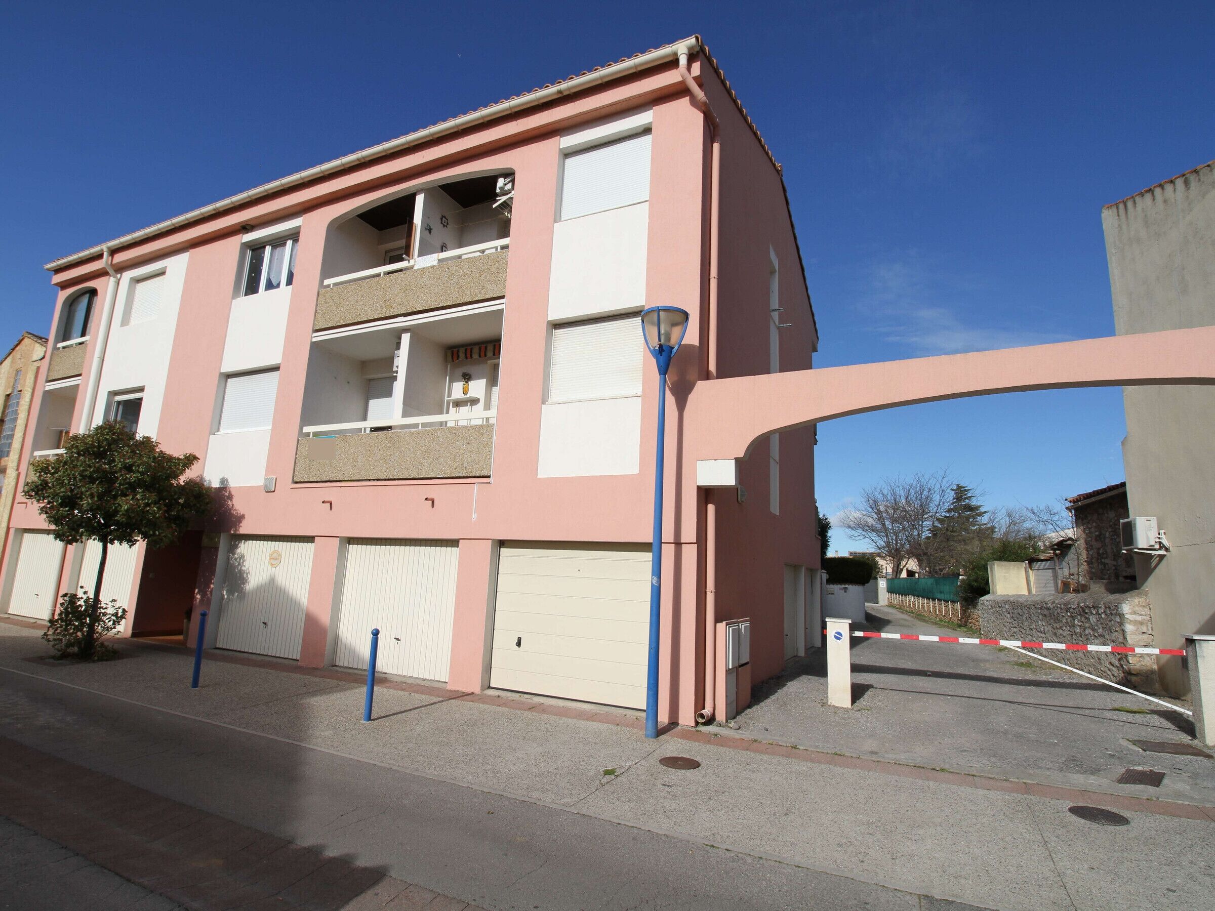 A multi-story residential building with balconies, a gated entrance, and a clear sky.