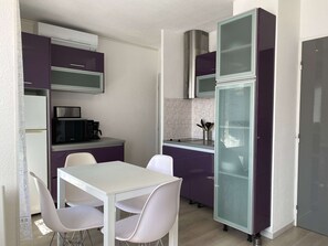 Una cocina pequeña con armarios morados, una mesa blanca y sillas.