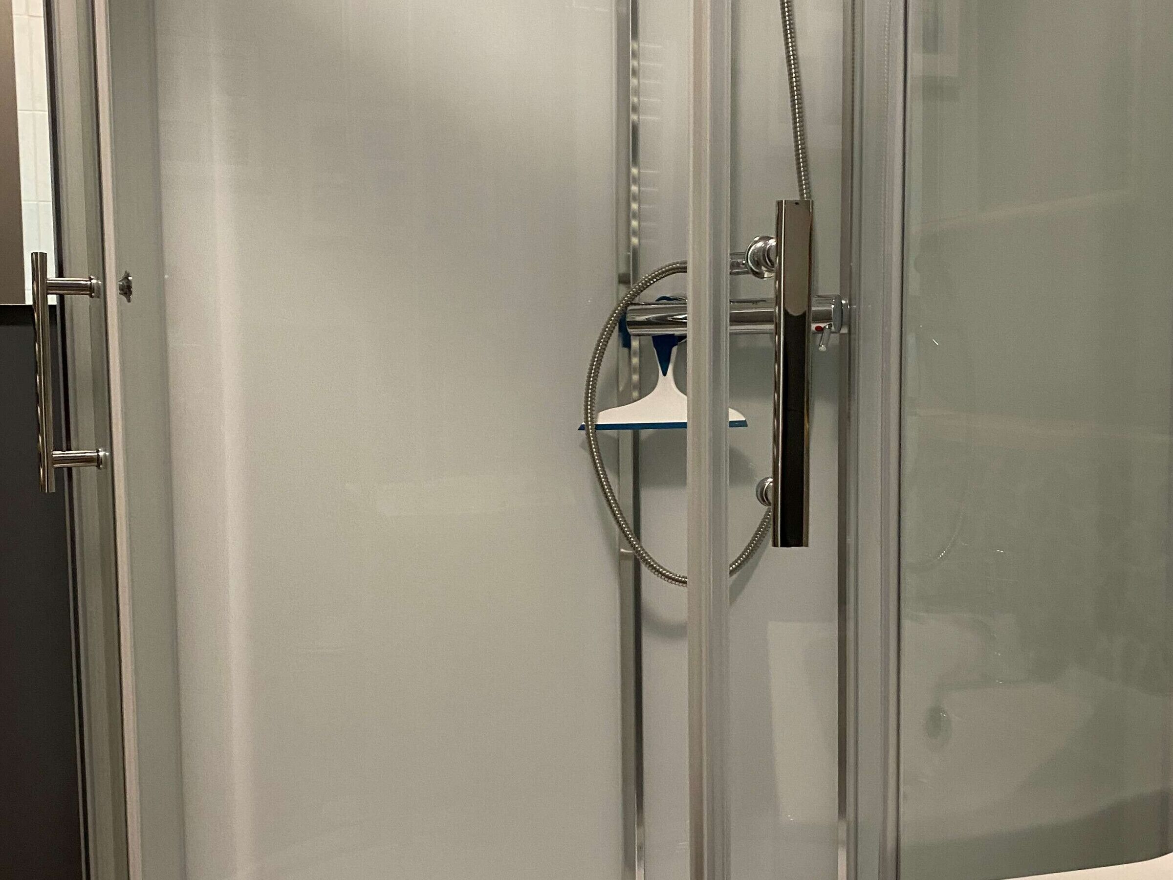 Un espace douche doté d’une porte en verre, d’un pommeau de douche à main et d’un porte-serviettes.