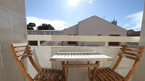 A small balcony with a white table and two wooden chairs. - Charming T2 Apartment with Private Garage and Balcony in Central Village (Balaruc-les-Bains)