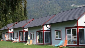 Eine Reihe von kleinen, einstöckigen Gebäuden mit großen Fenstern und flachem Dach, umgeben von einer Rasenfläche mit einigen Liegestühlen.