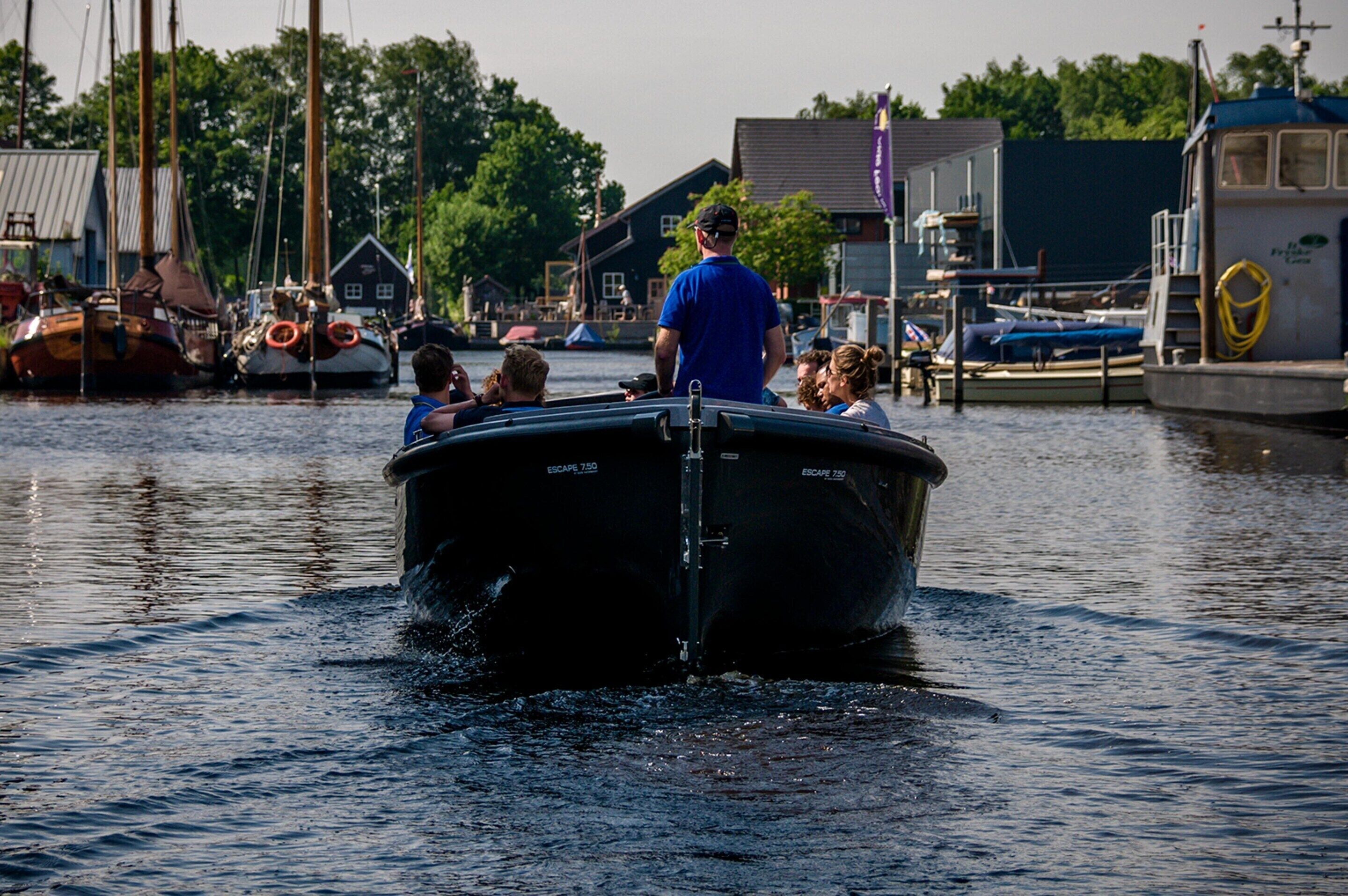 A boat with people on it, docked near buildings and trees.