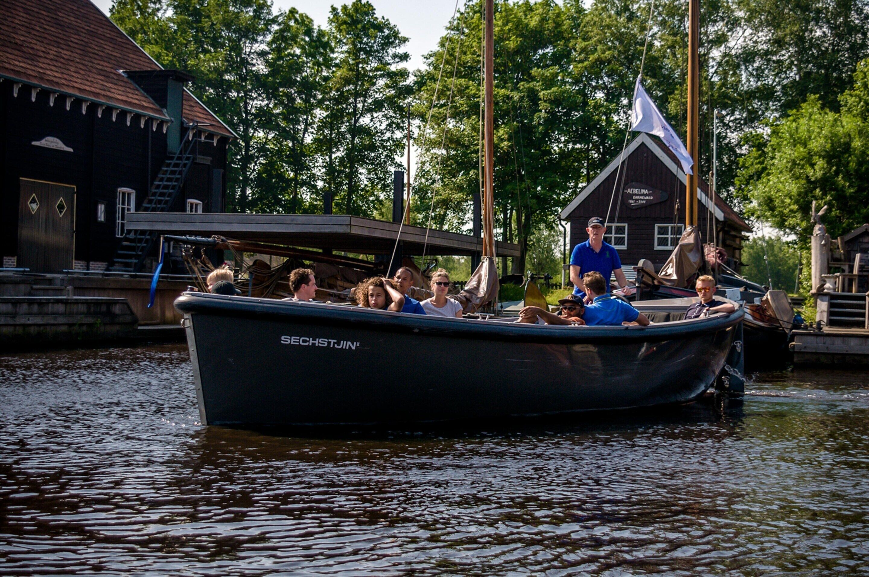 Ein Boot mit Personen am Ufer, nahe einem Gebäude mit dem Schild 'ACELINA'.