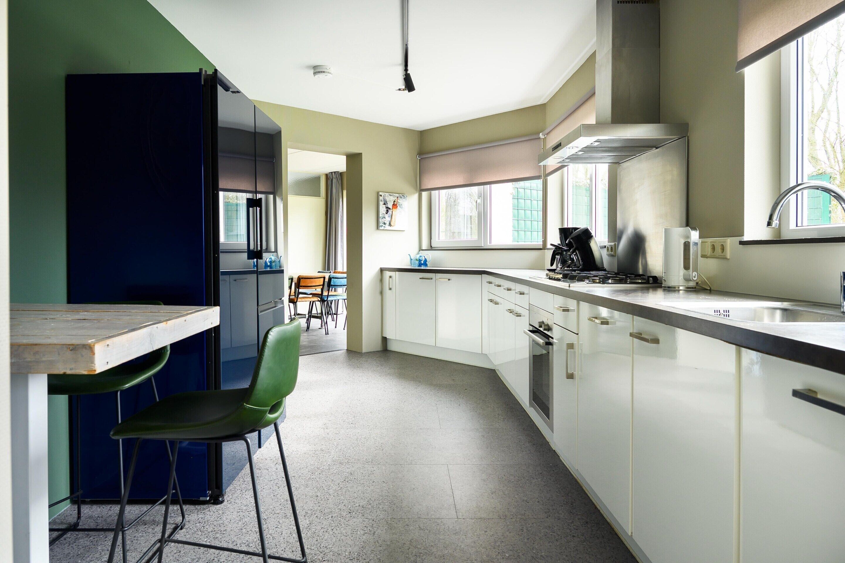Una cocina moderna con armarios blancos, un refrigerador negro y una silla verde.