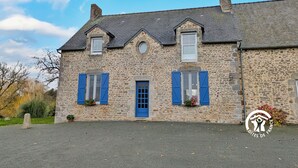 A stone building with a blue door and shutters, featuring a small garden area with potted plants.