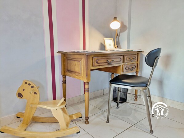 A wooden desk with drawers, a chair, and a rocking horse in a room with striped walls.