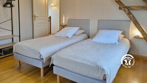 A bedroom with two single beds, a wooden bench, a wardrobe, and a staircase.