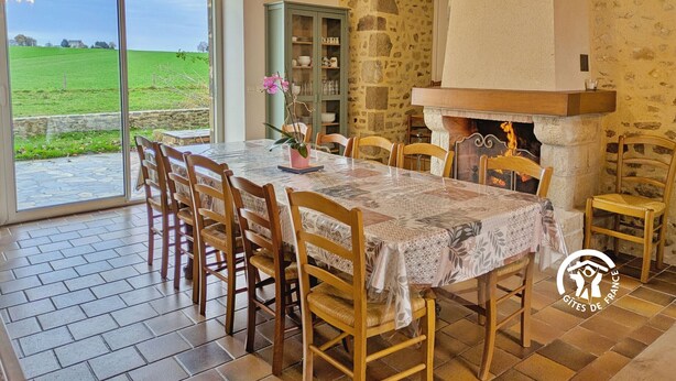 A dining area with a stone wall, a fireplace, and a view of a green field through a glass door.