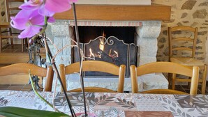 A cozy room with a fireplace, wooden chairs, and a table with patterned tablecloths.