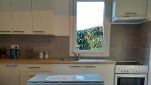 Eine Küche mit weißen Schränken, einem Fenster, einem eingebauten Backofen und einem blauen Tisch mit Schubladen.