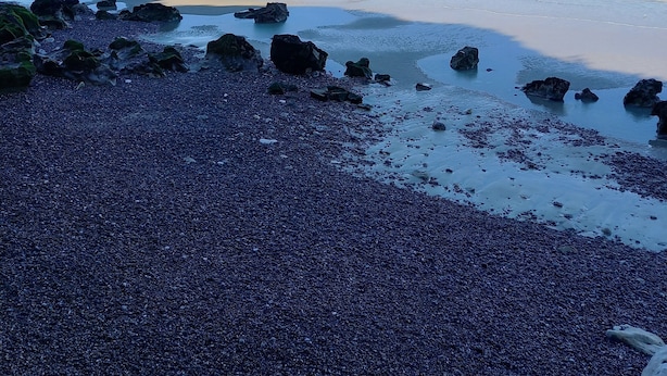 Ein Strand mit Kies und Felsen, ein Sandufer und ruhigem Wasser.