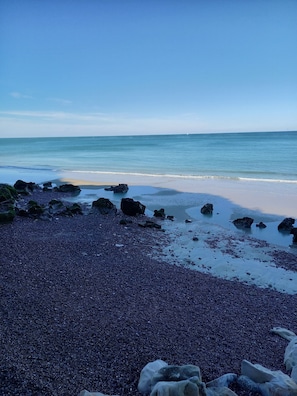 A beach with pebbles and rocks, a sandy shore, and calm water.