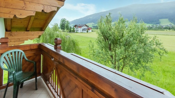 A wooden balcony with a view of a green field and a building in the distance. - Holiday Home in a Beautiful Location (Radstadt)