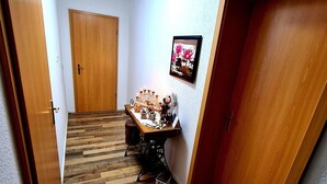 Un couloir étroit au plancher de bois, une machine à coudre et une petite table sur laquelle se trouvent divers objets.