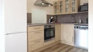 A modern kitchen with wooden cabinets, a stainless steel range hood, a built-in oven, a dishwasher, and a microwave. - Semi-detached house with private spa, pets welcome, near Cotentin (Saussemesnil)