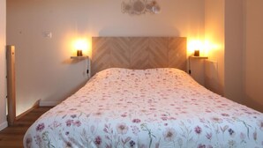 A bedroom with a floral bedspread, a wooden herringbone headboard, and wall-mounted sconces. - Semi-detached house with private spa, pets welcome, near Cotentin (Saussemesnil)