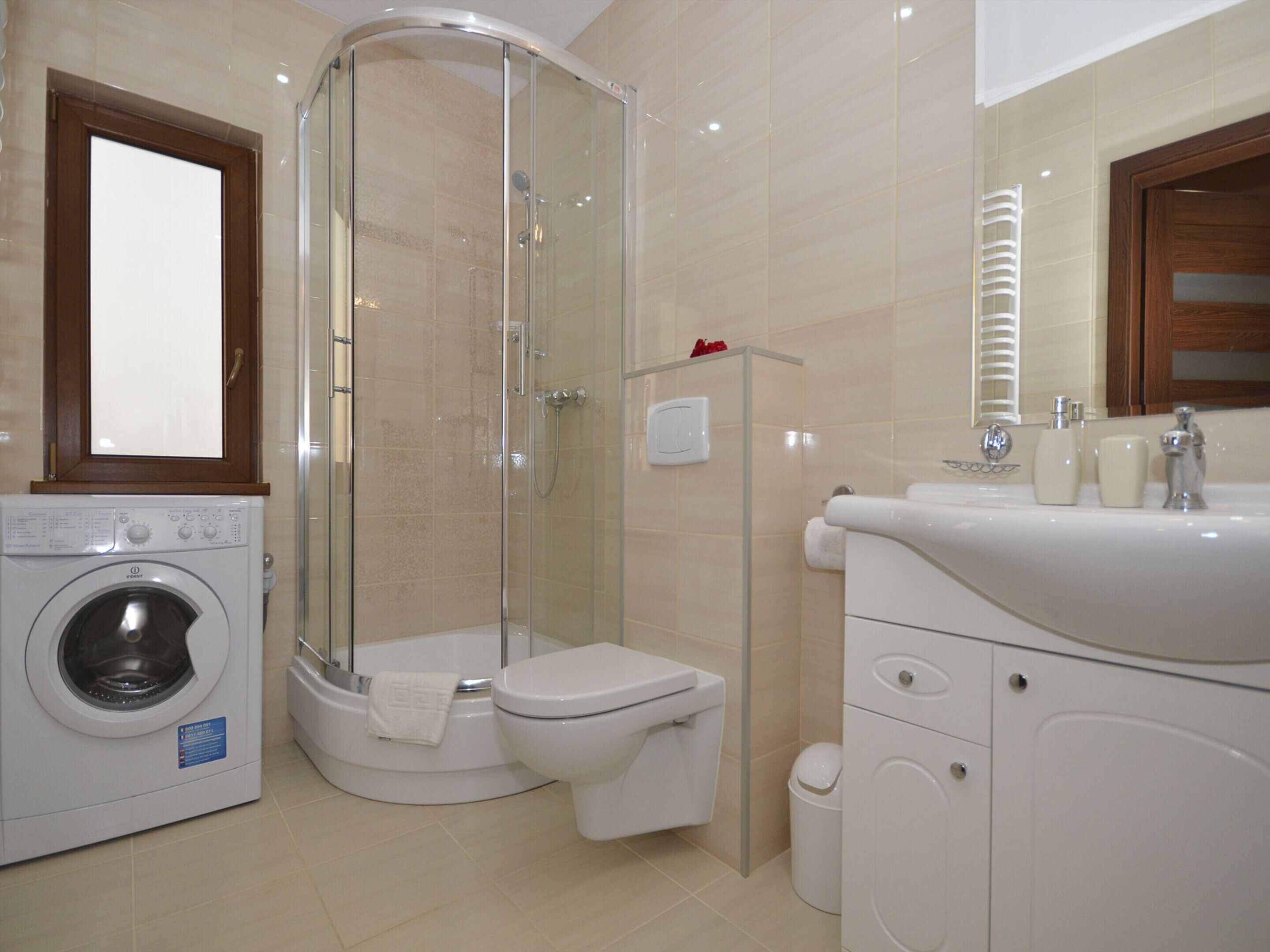Une salle de bain avec une douche en verre, des toilettes, un lave-linge et un lavabo équipé de produits de toilette.