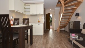 A modern kitchen with white cabinets, a dining table with chairs, and a wooden staircase. - Duplex Apartments 300 m From the Sea. Living Room, 2 Bedrooms, own Terrace (Darlowo)